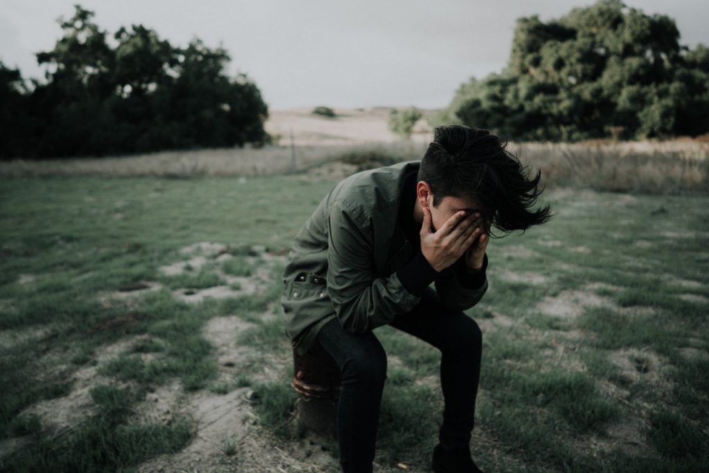 a mid aged boy sitting on the water covering his face with hands